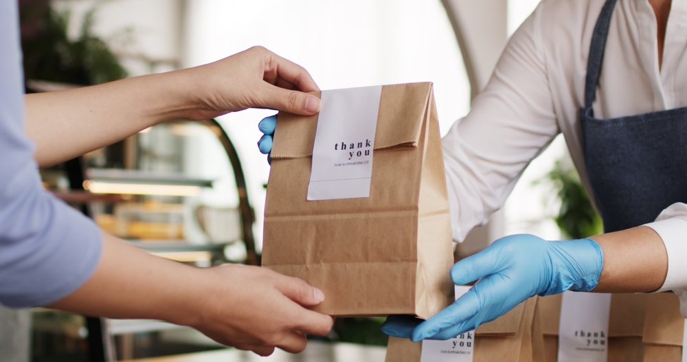 A customer receiving a brown paper takeaway bag from a shop worker.